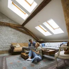 Para spędza czas w przytulnym salonie pod dachem wielospadowym, z widocznymi drewnianymi belkami i oknami dachowymi.