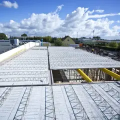 Budowa nowego stropu nad halą przemysłową. Metalowe kratownice i betonowe płyty tworzą solidną konstrukcję.