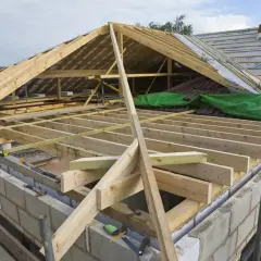 Budowa dachu w toku. Widoczna drewniana konstrukcja, wiatrownica i materiały budowlane.
