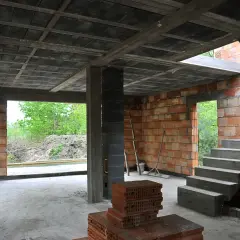 Wnętrze budowy z widocznymi stropy gęstożebrowe, betonowymi schodami i ceglanymi ścianami.