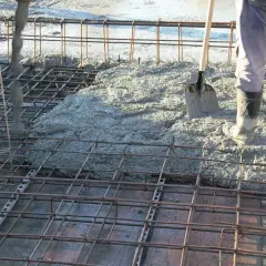 Betonowanie stropu. Robotnicy w gumowcach wylewają beton na zbrojenie. Łopata czeka na pomoc.