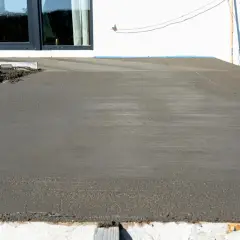 Świeżo wylany taras betonowy, gotowy na letnie wieczory. Obok okna i biała ściana.