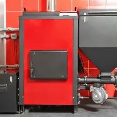 Nowoczesny piec na pellet do domu 120m2. Czerwono-czarna, kompaktowa jednostka z zasobnikiem na pellet i elementami instalacji.