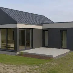 Nowoczesny dom z płyty warstwowej z dużymi przeszkleniami i betonowym tarasem.