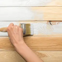 Ręka maluje białą farbą drewnianą boazerię. Proces odnawiania wnętrza.