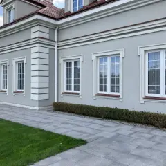 Elegancki budynek z jasnoszarym tynkiem, ozdobiony białymi pilastrami i gzymsami. Okna z białymi ramami i brązowymi parapetami.