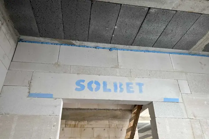 Dylatacja między stropem a ścianą z bloczków SOLBET, wypełniona pianką. Widoczne szare bloczki stropowe i białe bloczki ścienne.