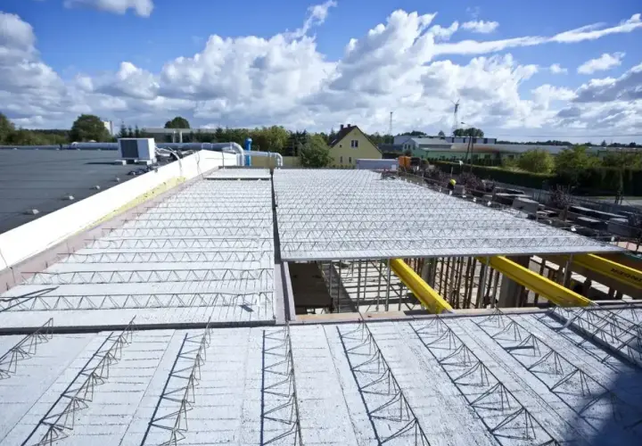 Budowa nowego stropu nad halą przemysłową. Metalowe kratownice i betonowe płyty tworzą solidną konstrukcję.