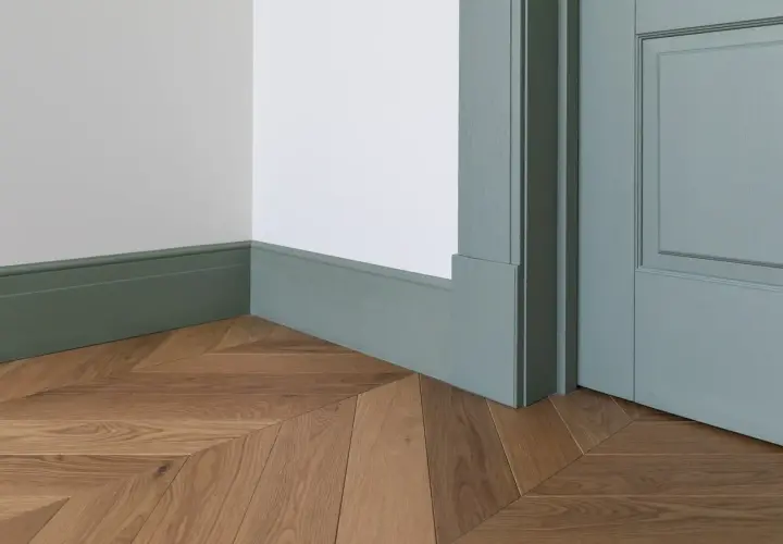 Eleganckie, zielone cokoliki idealnie komponują się z drewnianą podłogą ułożoną we wzór jodełki.