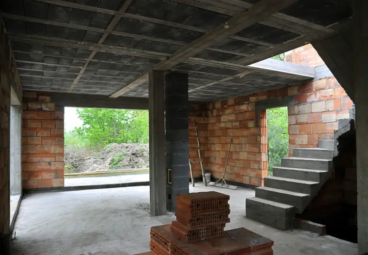 Wnętrze budowy z widocznymi stropy gęstożebrowe, betonowymi schodami i ceglanymi ścianami.