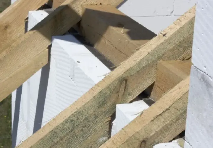Drewniana konstrukcja dachu z belkami i murłatą opiera się na białych bloczkach z betonu komórkowego.