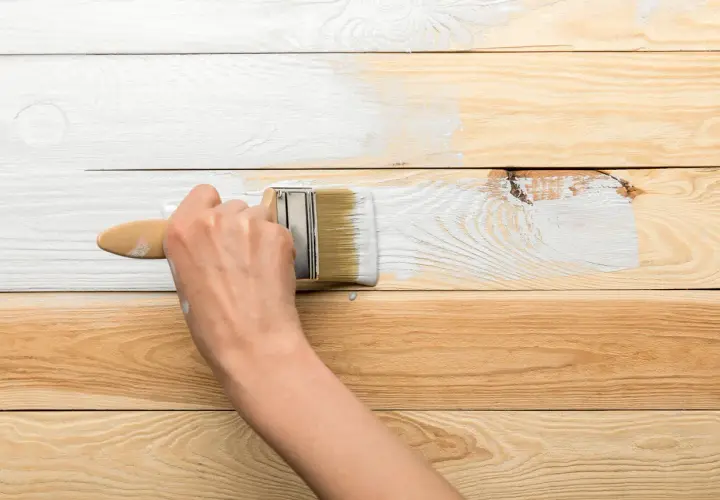 Ręka maluje białą farbą drewnianą boazerię. Proces odnawiania wnętrza.
