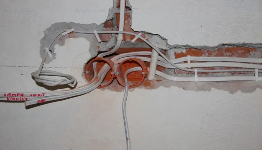Rozpoczęta wymiana instalacji elektrycznej: widoczne puszki, przewody i fragmenty ceglanej ściany.