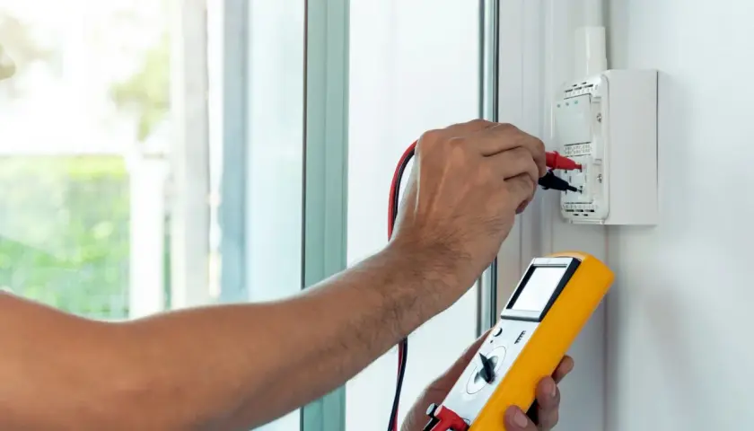 Elektryk mierzy impedancję pętli zwarcia za pomocą żółtego miernika.