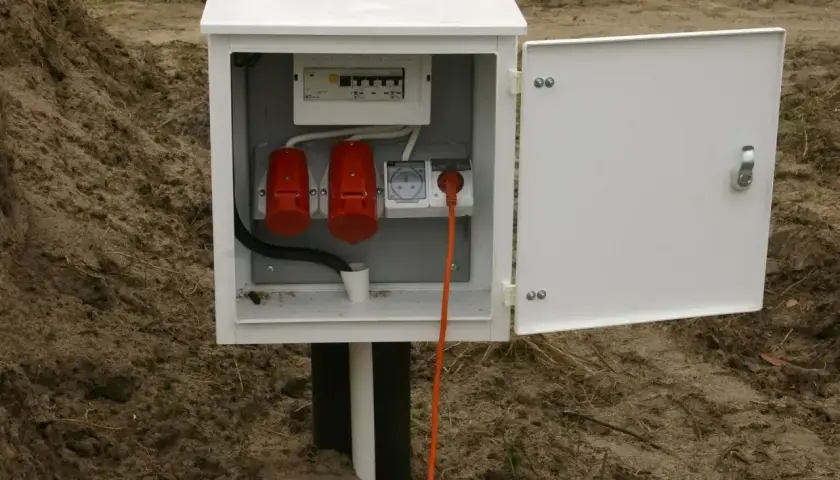 Skrzynka elektryczna na działce bez domu, z bezpiecznikami i gniazdami, gotowa na podłączenie prądu.