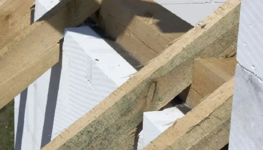 Drewniana konstrukcja dachu z belkami i murłatą opiera się na białych bloczkach z betonu komórkowego.