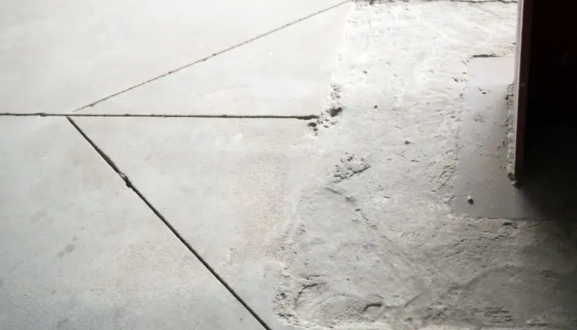 Szara posadzka z widoczną dylatacją. W jednym miejscu beton jest uszkodzony, odsłaniając podłoże.