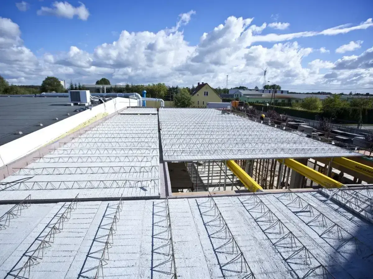 Budowa nowego stropu nad halą przemysłową. Metalowe kratownice i betonowe płyty tworzą solidną konstrukcję.