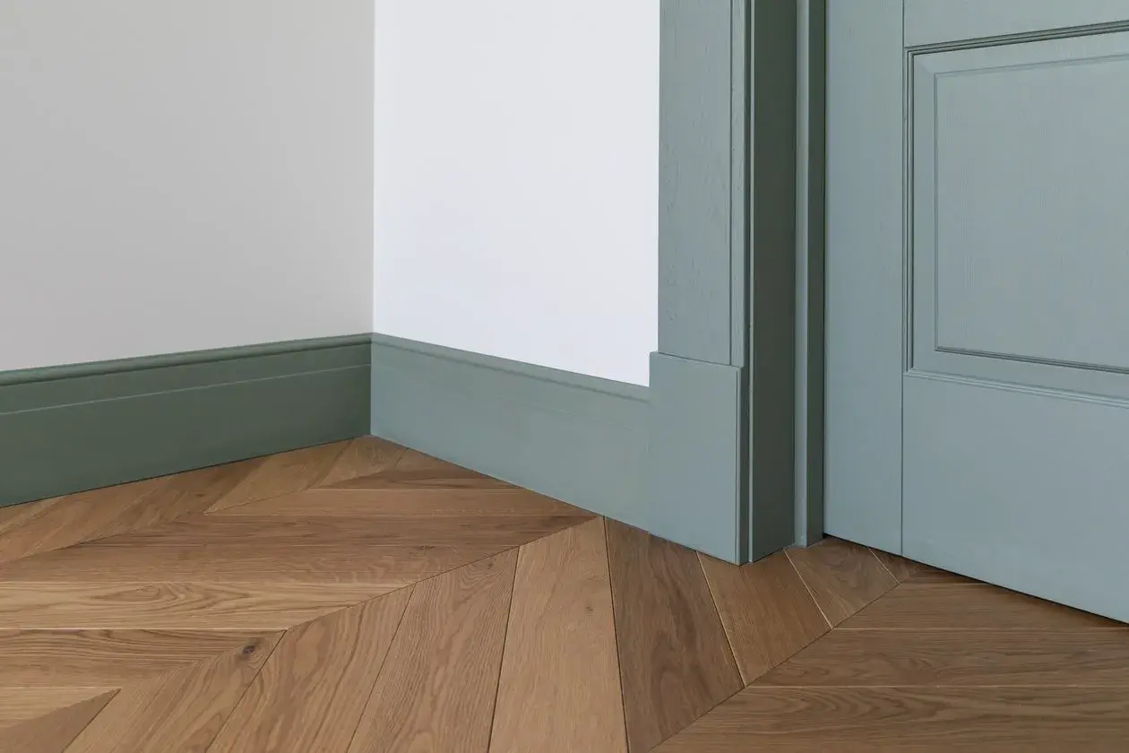 Eleganckie, zielone cokoliki idealnie komponują się z drewnianą podłogą ułożoną we wzór jodełki.