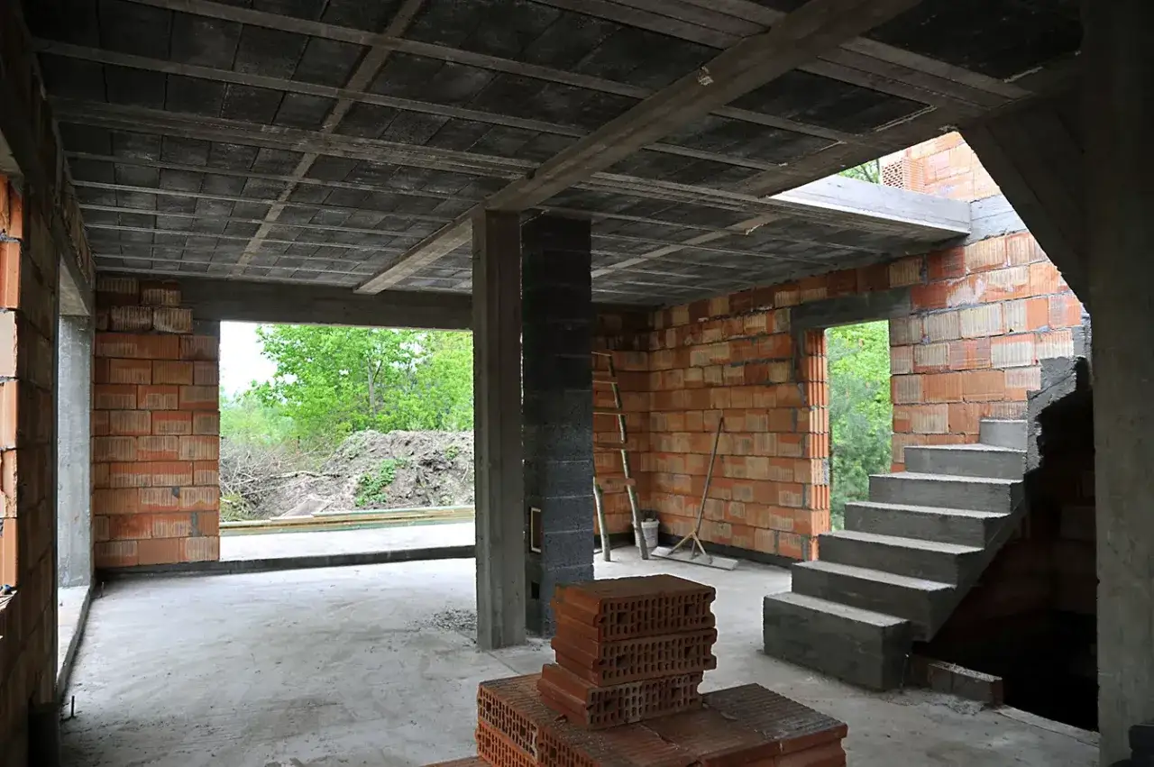 Wnętrze budowy z widocznym stropem ackermana, schodami i ceglanymi ścianami.