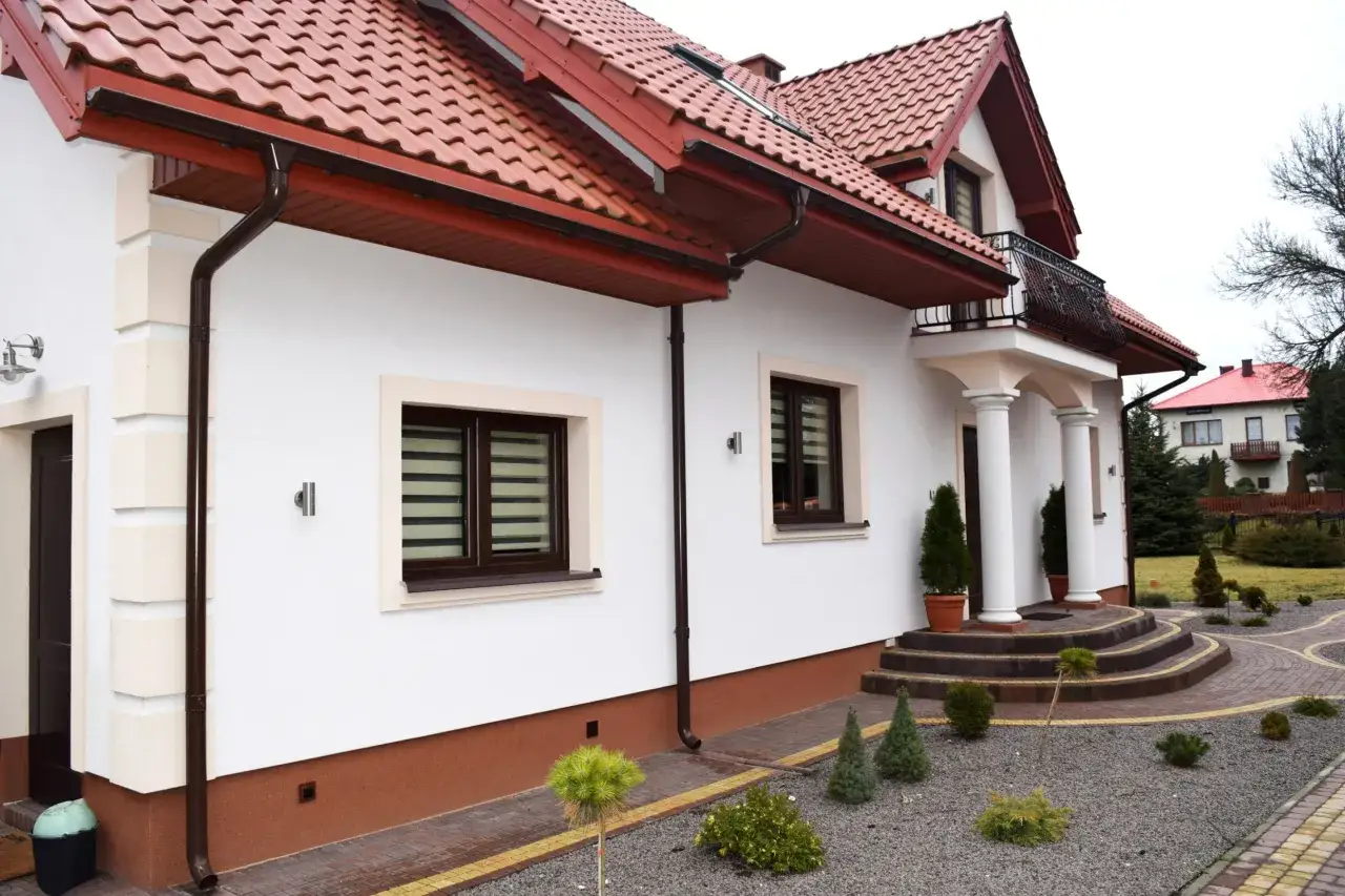 Elegancki cokół na elewacji domu, wykończony brązową tynkowaną powierzchnią, chroni ściany przed wilgocią.