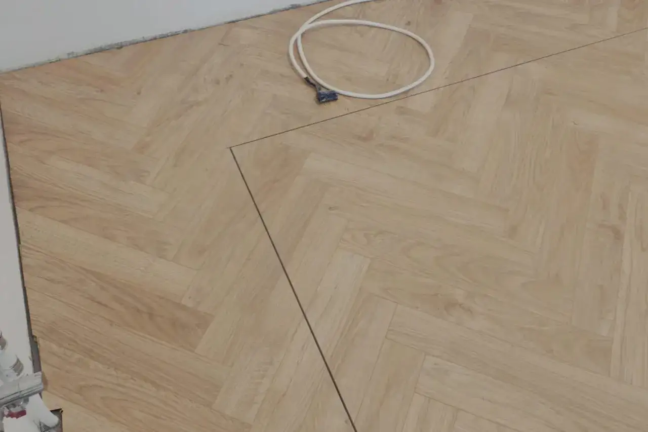 Układanie paneli w kuchni w jodełkę. Widać biały kabel i czarną linię wyznaczającą cięcie.